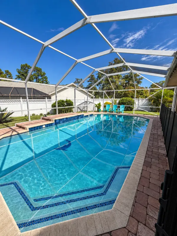 Screen-enclosed pool with a dolphin mosaic and mirror-clear water reflecting the enclosure